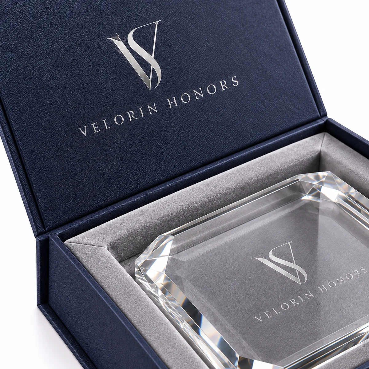 Close-up of silver foil branding on a textured navy rigid award box beside a gray velvet insert and faceted crystal edge.