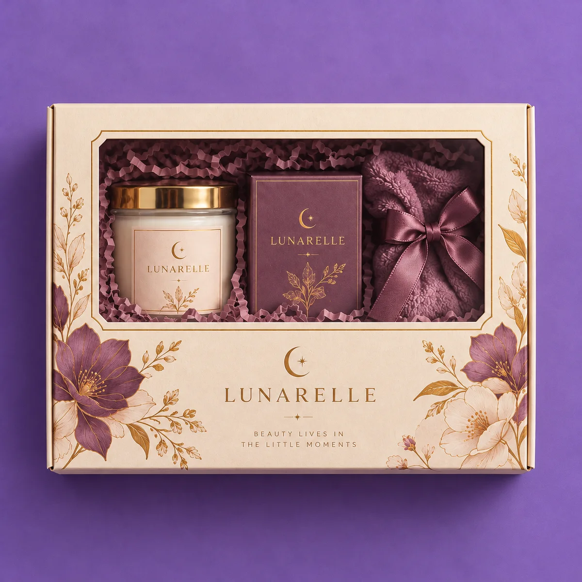 Overhead view of a cream window gift box with gold-bordered floral packaging, a candle jar, gift carton, and ribbon-wrapped cloth.