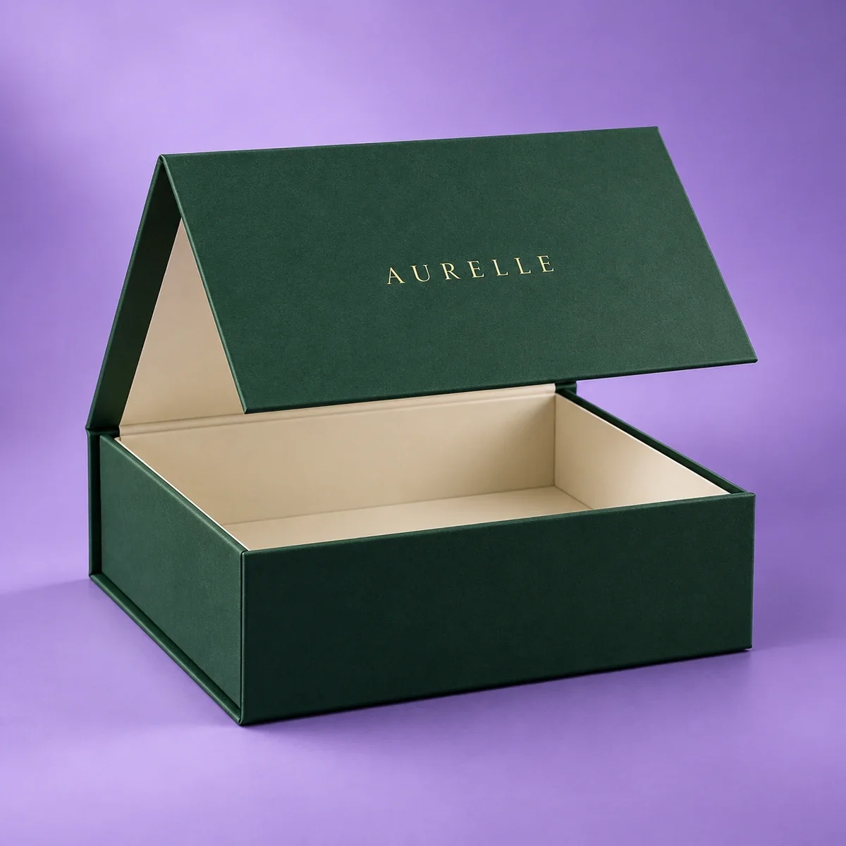 Custom magnetic gift box in emerald green with gold AURELLE lettering, ivory interior, and partially open hinged lid