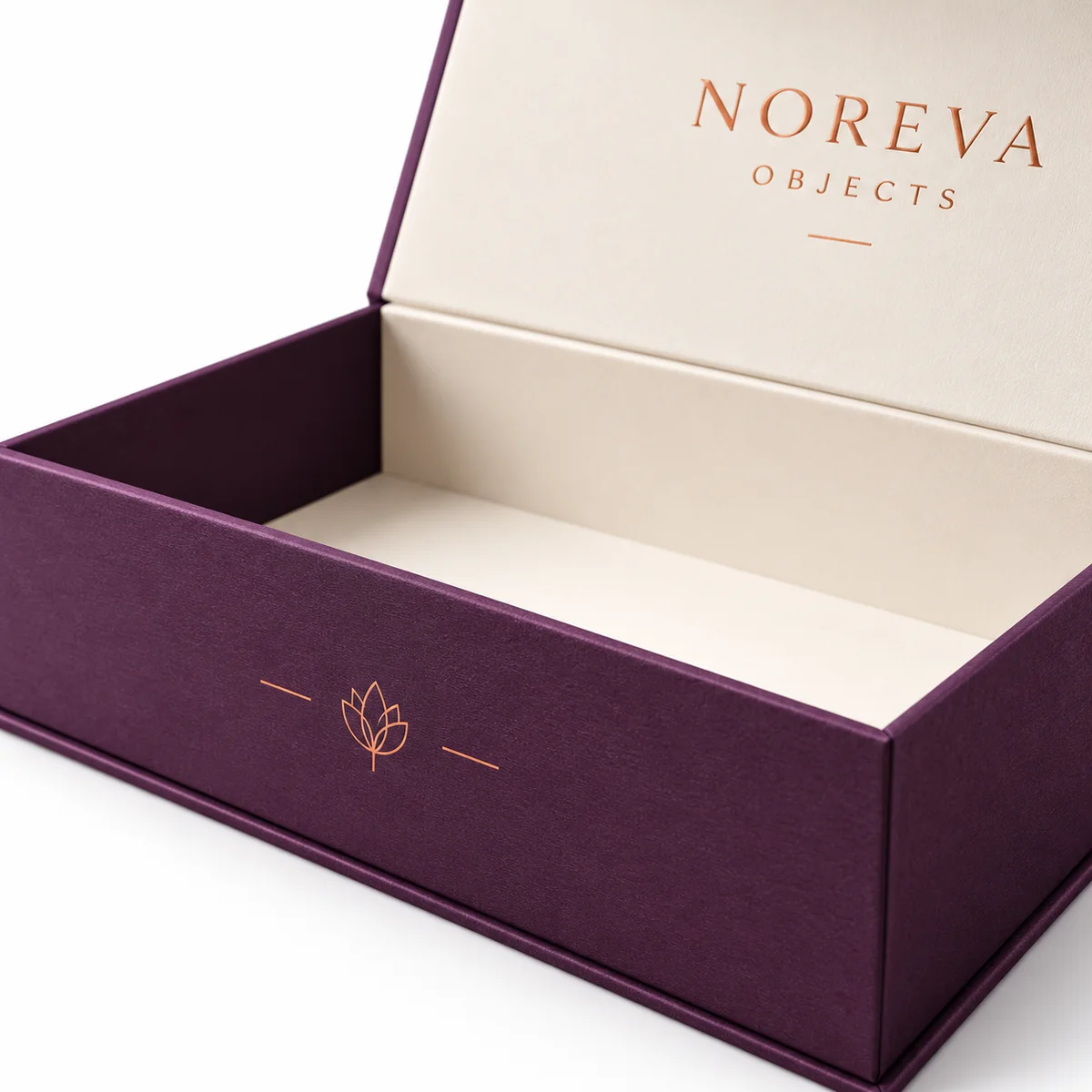 Close-up of a plum magnetic closure box showing textured paper wrapping, copper floral emblem, crisp edges, and ivory lining.