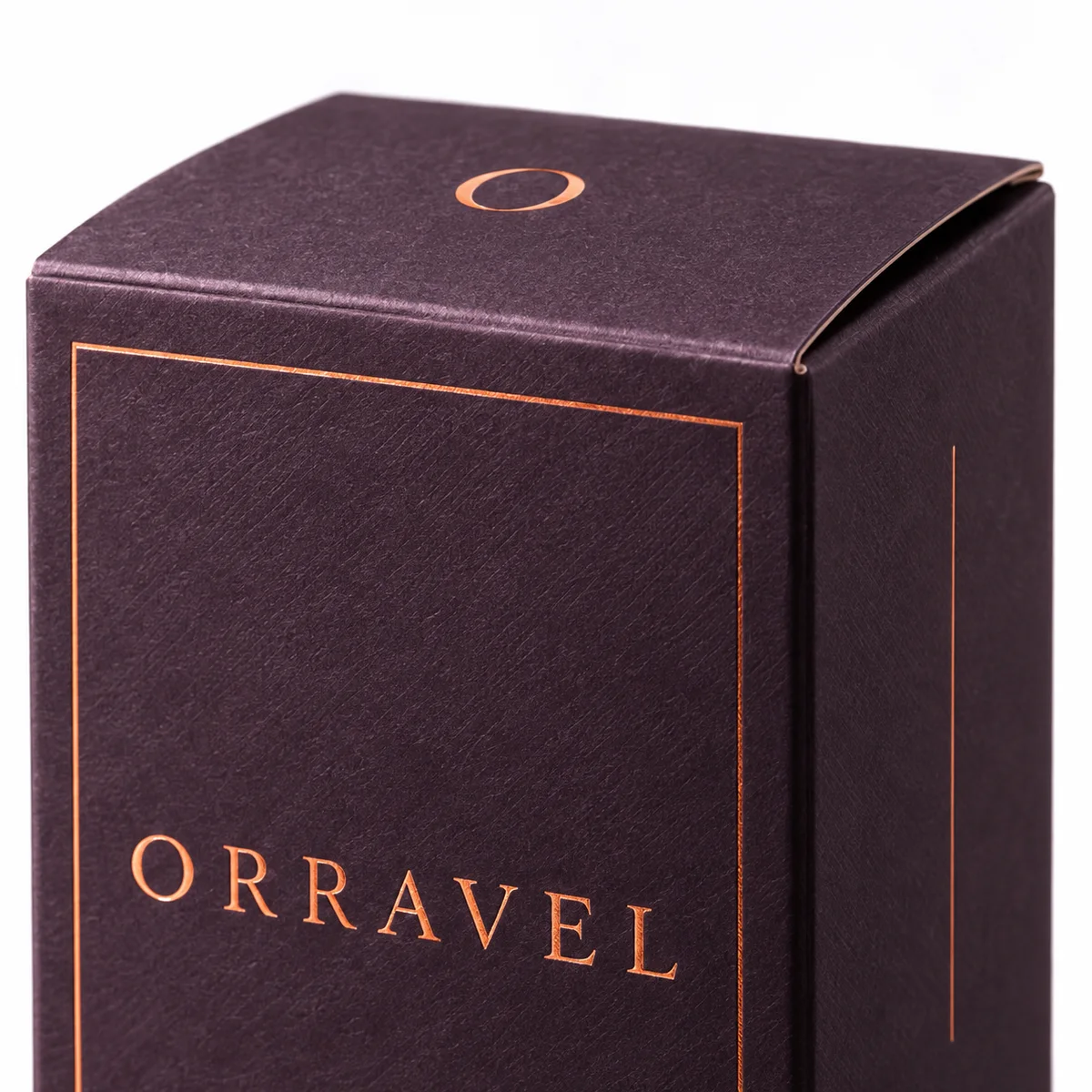 Macro view of a plum reverse tuck end box showing its folded top edge, copper monogram, and textured surface.