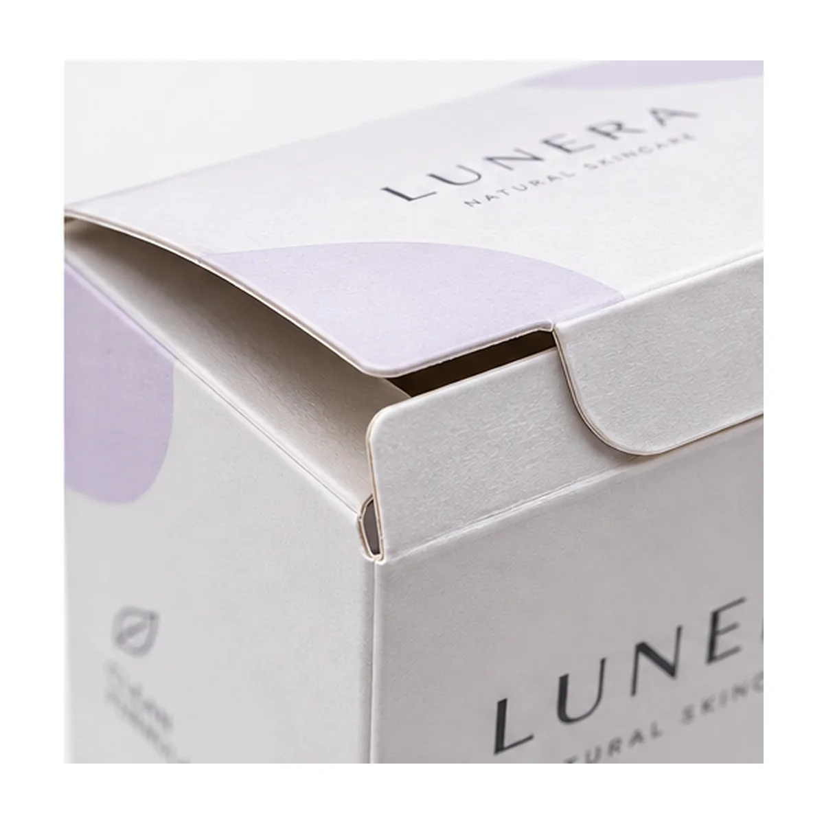 Close-up of a white tuck top box showing the partially opened flap, folded paperboard edges, lavender graphics, and LUNERA branding.