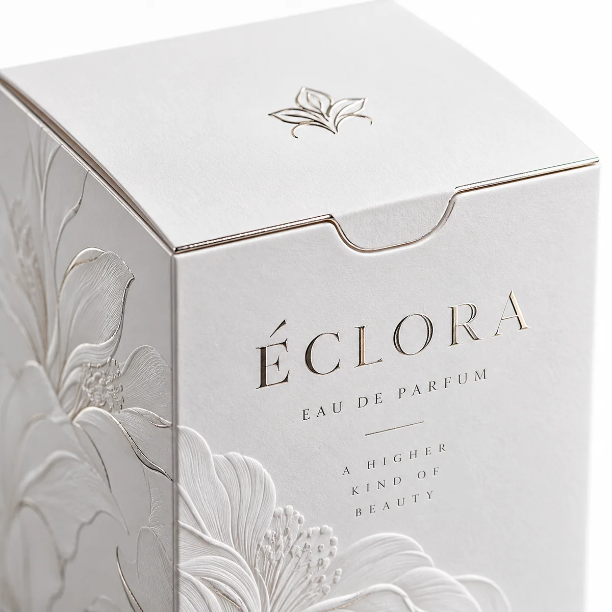 Close-up of white tuck top fragrance packaging with ÉCLORA lettering, metallic detailing, and raised floral patterns.